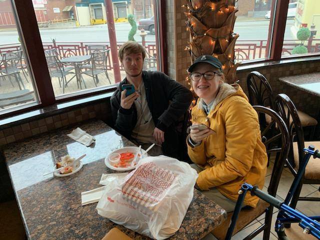 two students smiling for the camera while sitting at a table in a bakery